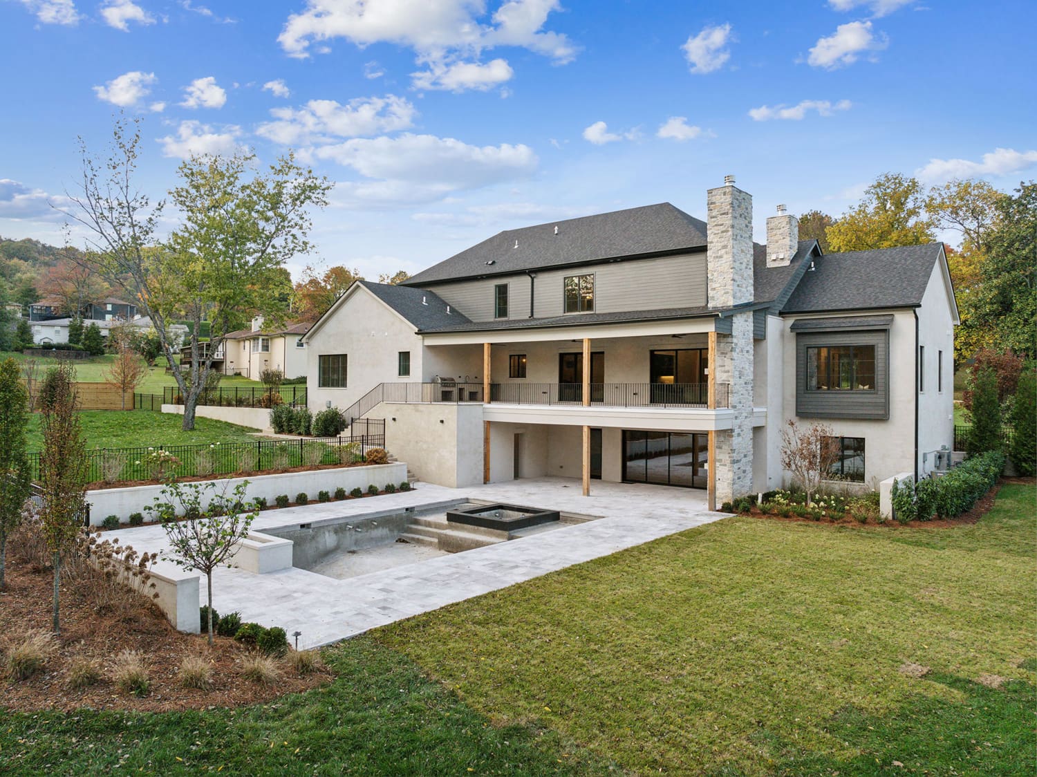Two-story modern house with covered balcony, stone chimneys, large windows, patio, and empty pool.