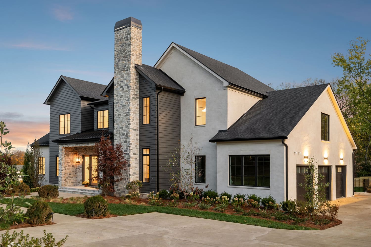 Two-story house with dark siding, light stucco, stone chimney, large windows, and three-car garage.