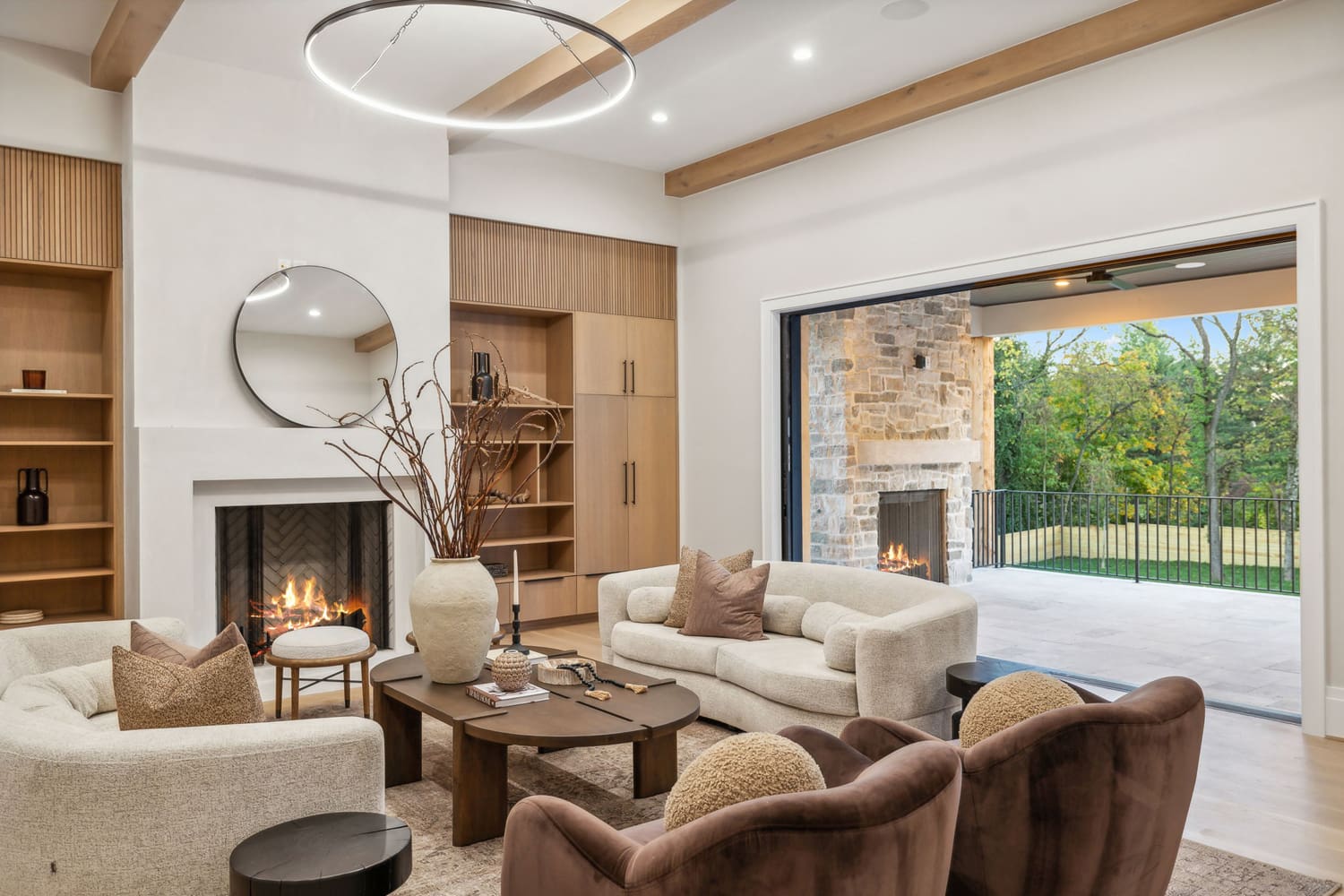 Living room with neutral sofas, wooden coffee table, fireplaces, and open patio with stone fireplace.