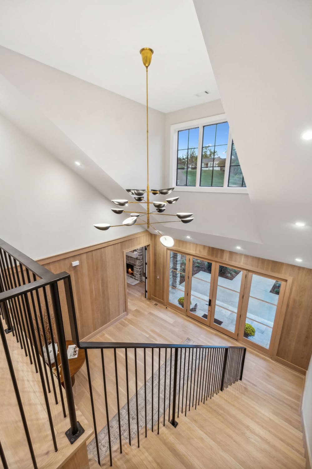 Modern entryway with wood flooring, black metal railing, large windows, glass doors, and gold chandelier