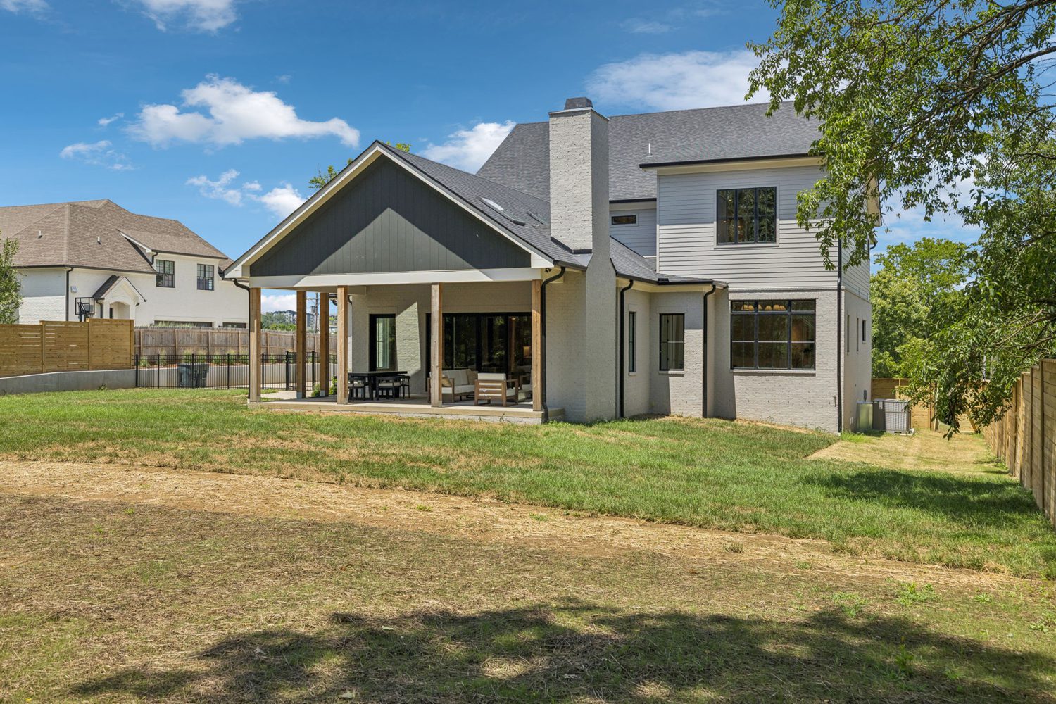 Two-story house with covered patio, outdoor furniture, fenced grassy backyard, and chimney.