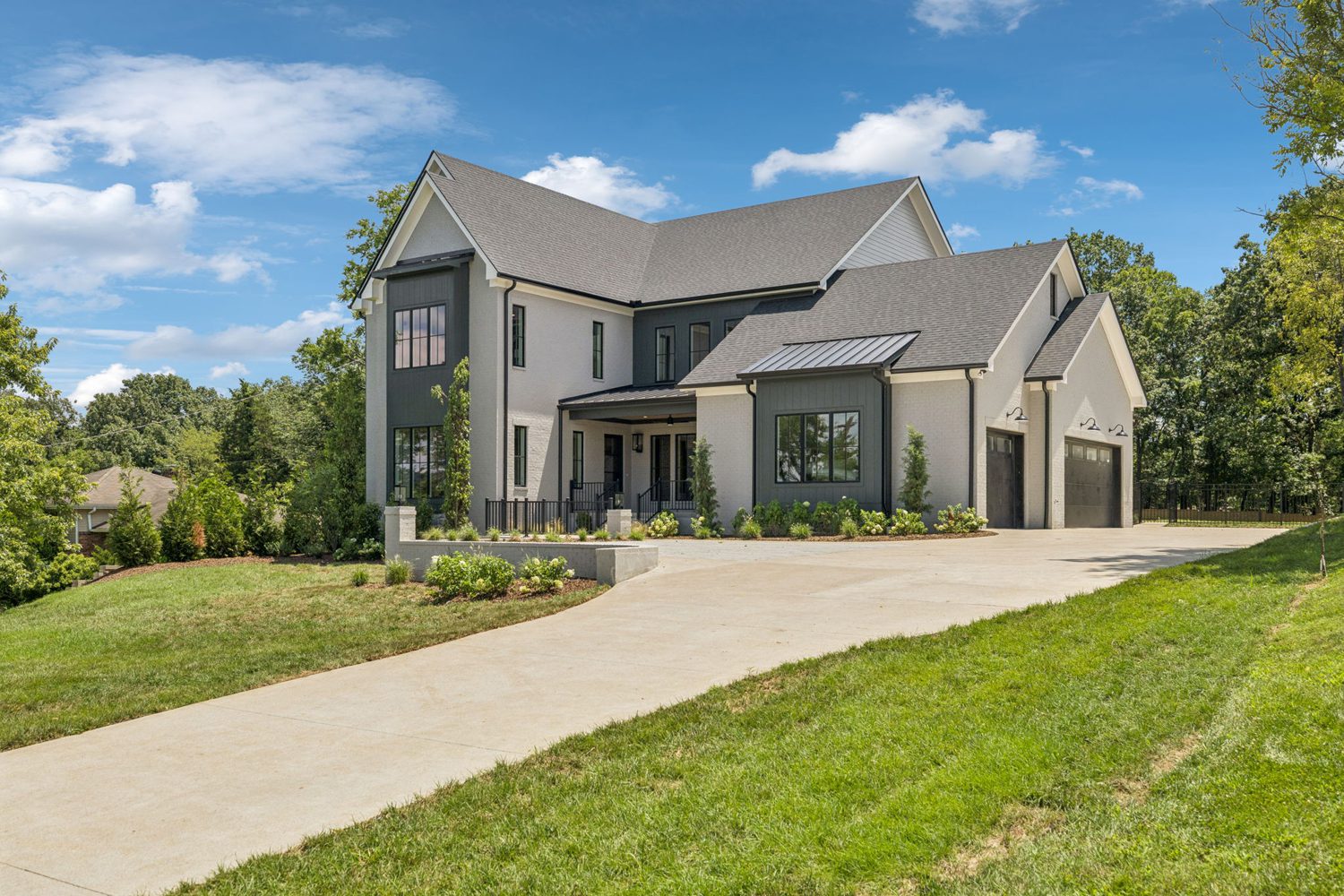 Two-story modern house with gray roof, light and dark walls, three-car garage, and landscaped yard.
