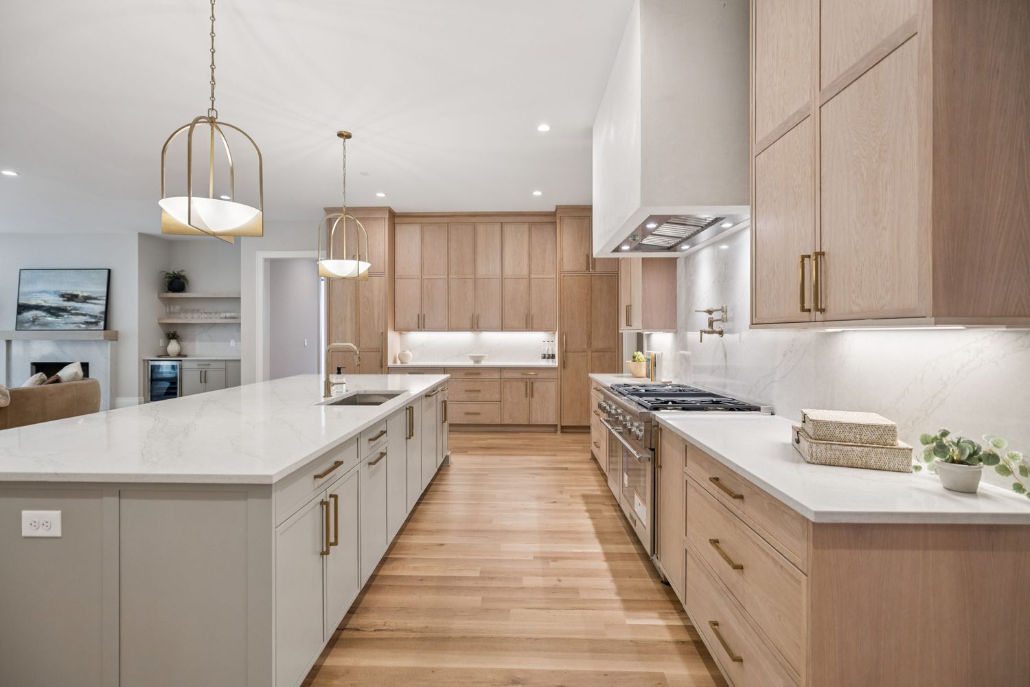 Modern kitchen with light wood cabinets, white countertops, large island, stainless stove, and pendant lights.
