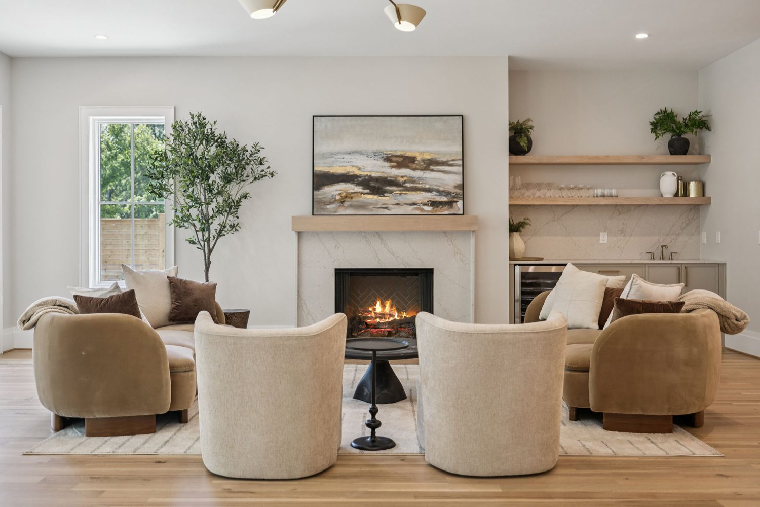 Living room with fireplace, abstract painting, beige and brown chairs, shelves, and large window.