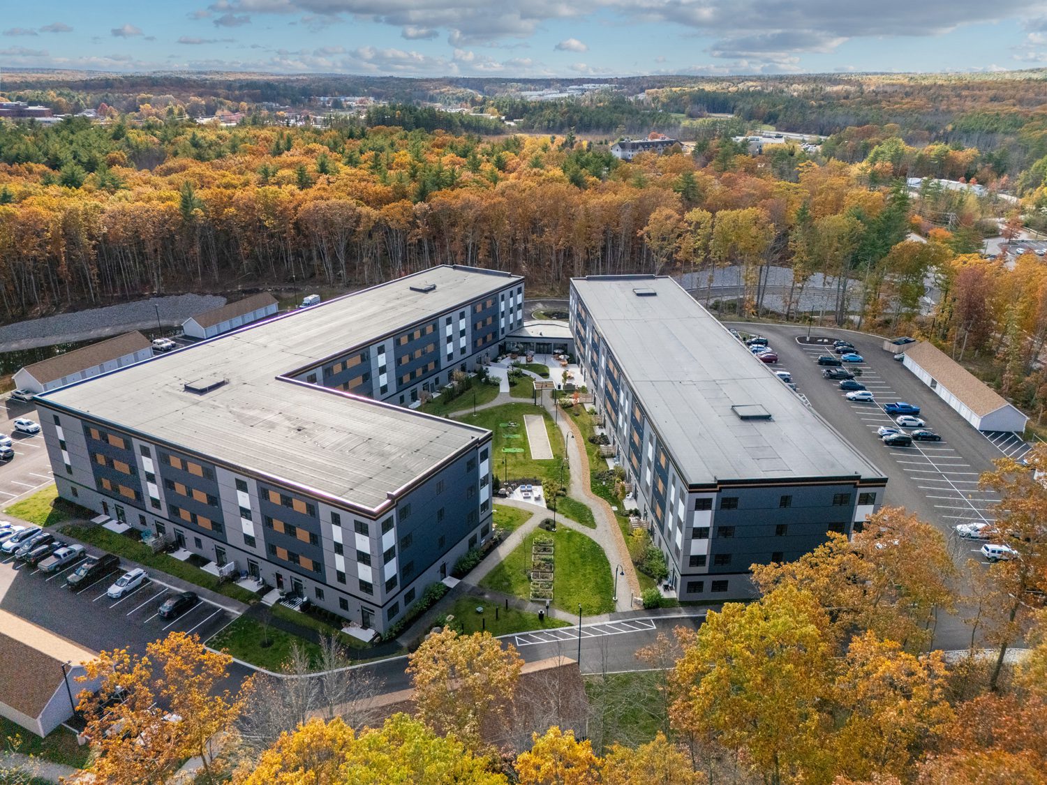 Aerial view of L-shaped modern apartment buildings with central courtyard and autumn trees nearby.