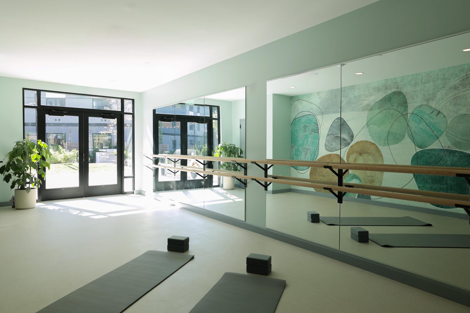 Exercise room with large windows, mirrored wall, wooden ballet barres, mats, blocks, and mural.