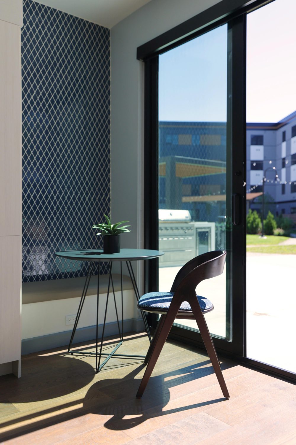 Small indoor seating with a wooden chair and round table by glass sliding door and blue tiled wall.