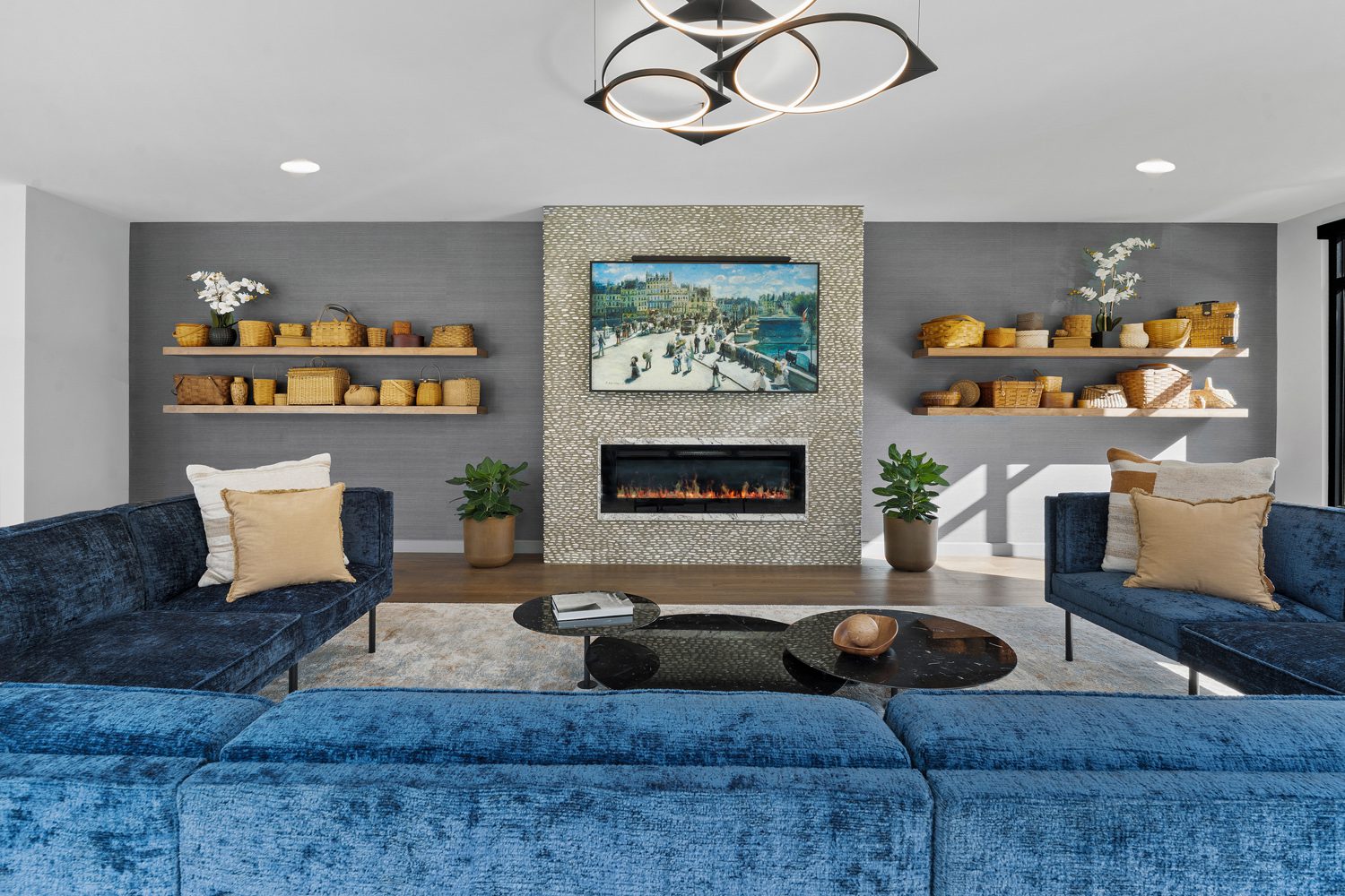 Living room with blue velvet sofas, black round coffee tables, fireplace, wall art, and shelves with baskets.