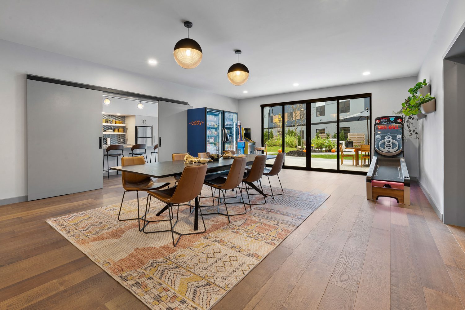 Dining area with six brown chairs, patterned rug, vending machine, arcade and skee-ball games.