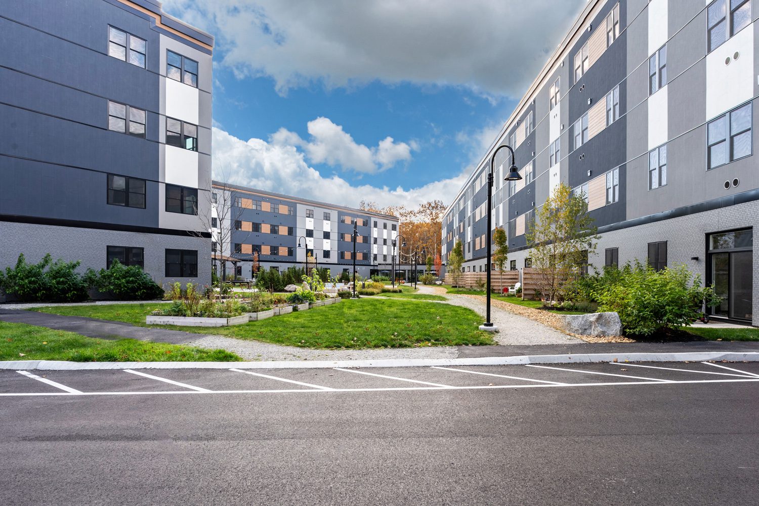 Modern four-story residential buildings surround a landscaped courtyard with pathways and greenery.